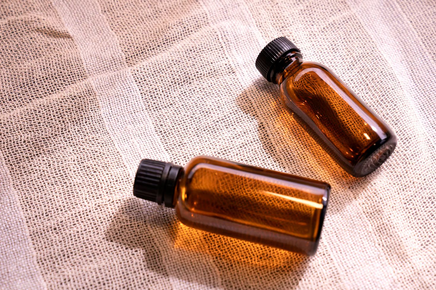 Two small amber glass bottles with black caps lying on loosely woven cloth