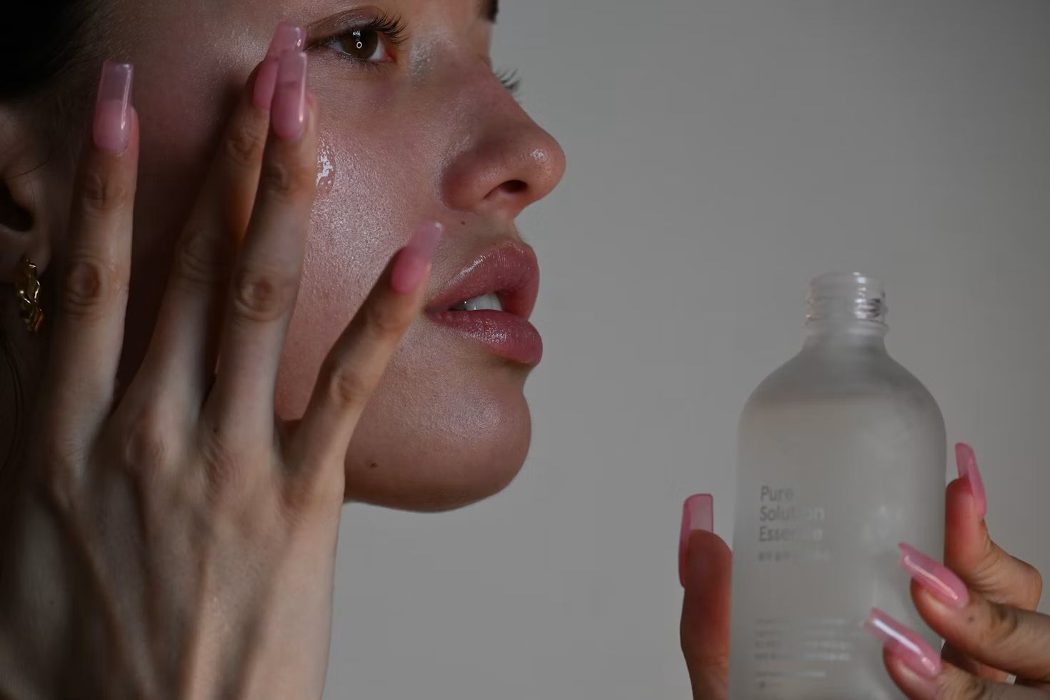 Woman touching her cheek while holding a frosted glass skincare bottle.